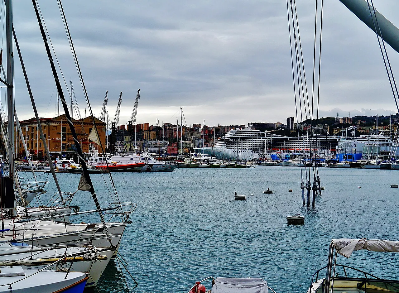 Sailboats moored in the Porto Antico of Genoa with a cruise ship and the hillside city behind